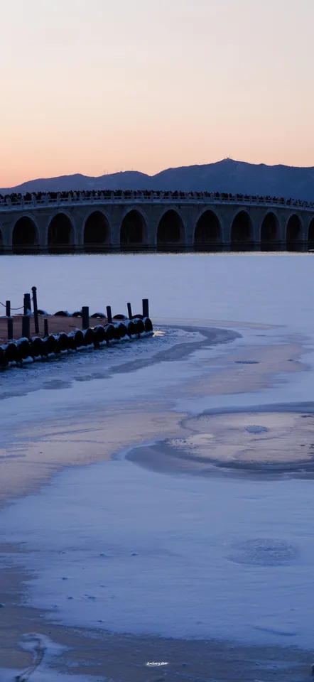 Bridge arches beside a frozen lake in evening light
