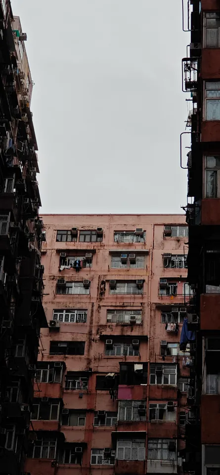 A pink apartment building between shadowed towers